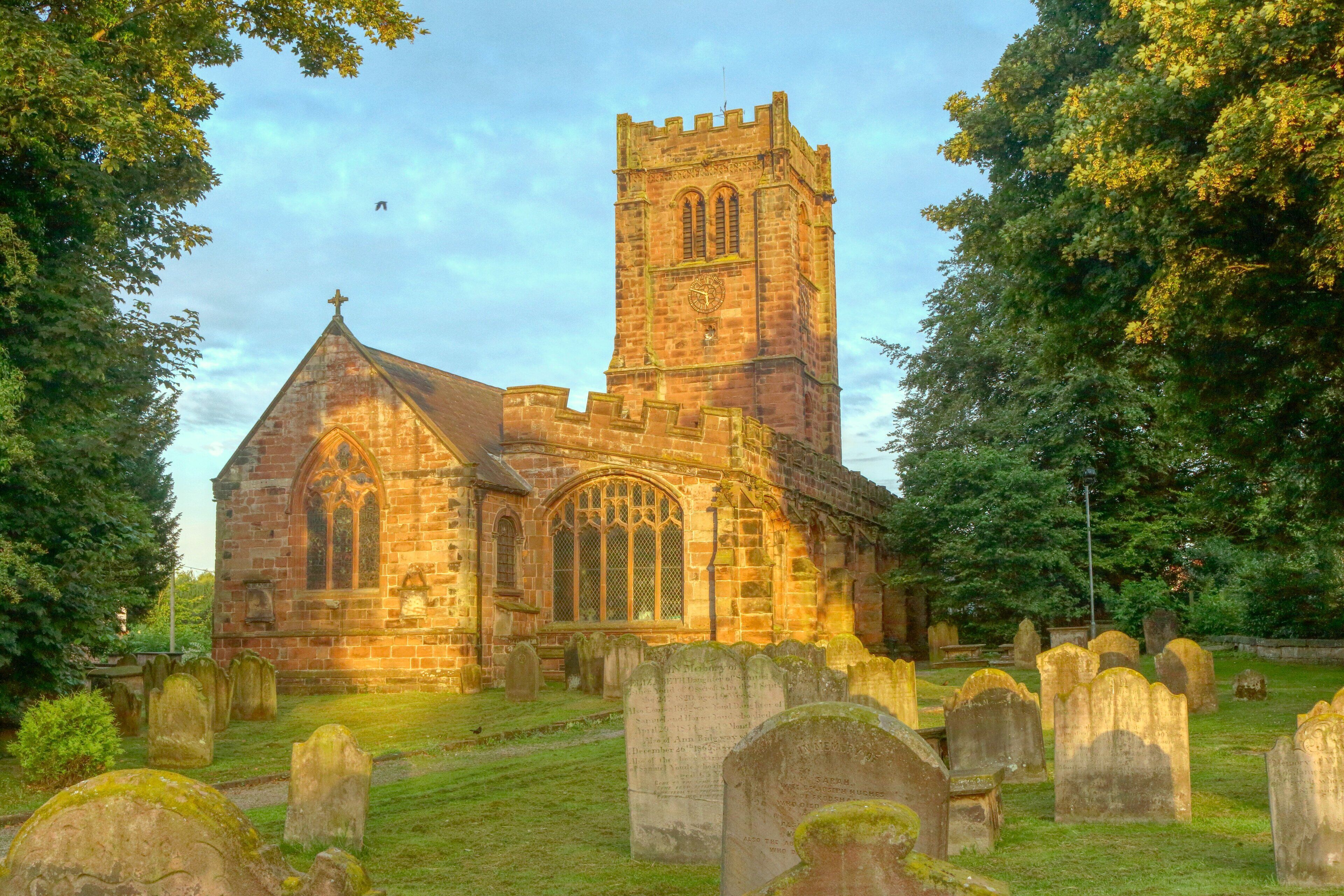 A historic church with a tall tower and a cemetery in the foreground.