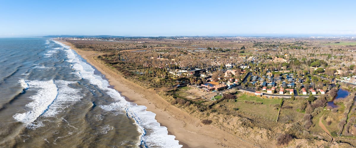 Un pueblo costero con playa, zona residencial y colinas al fondo.