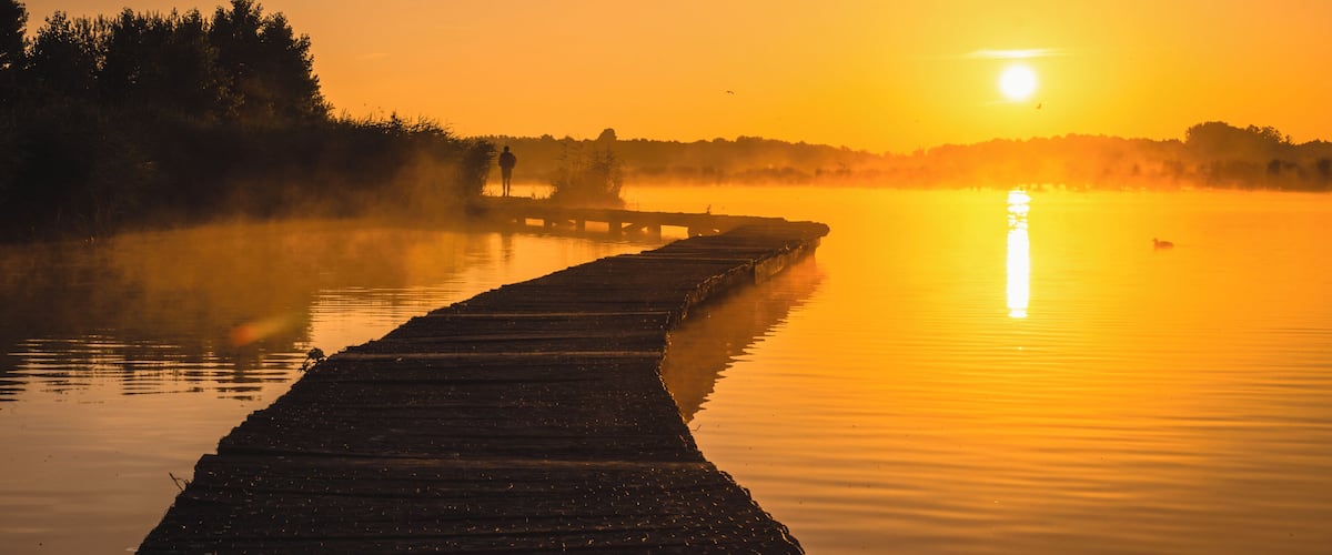 A wooden pier extending into calm water at sunrise.