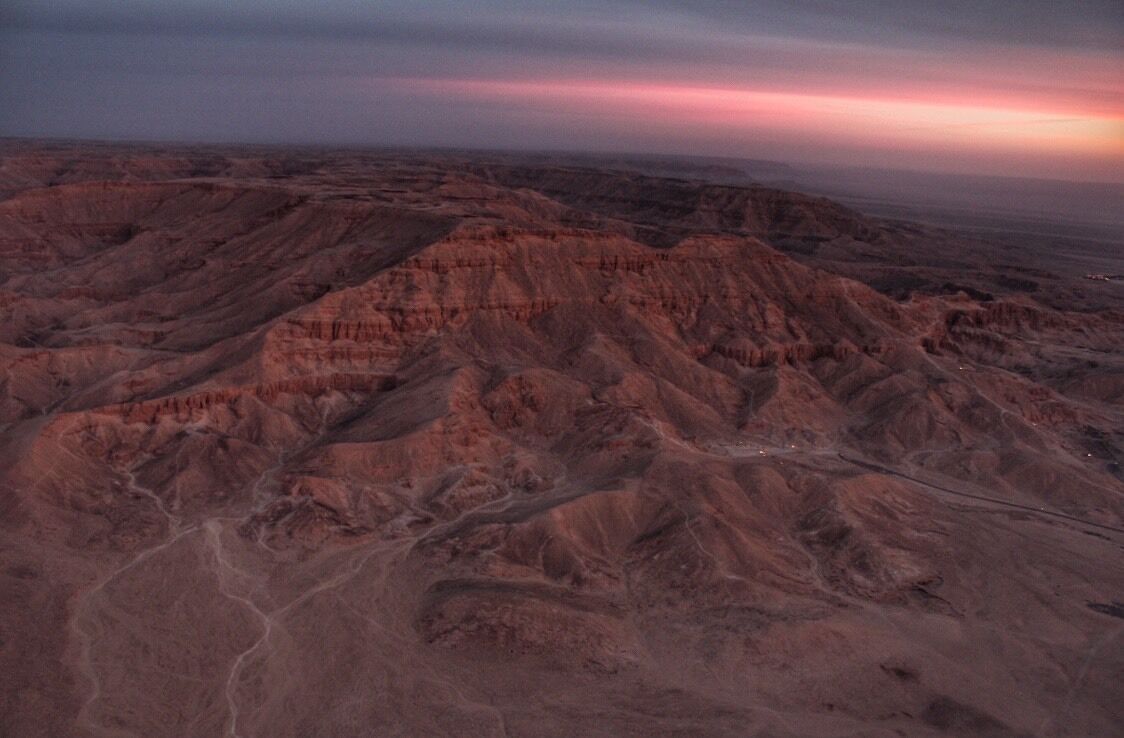 A rugged, eroded landscape with layered rock formations and a winding road.