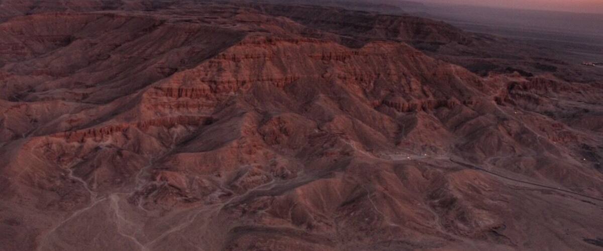 A rugged, eroded landscape with layered rock formations and a winding road.