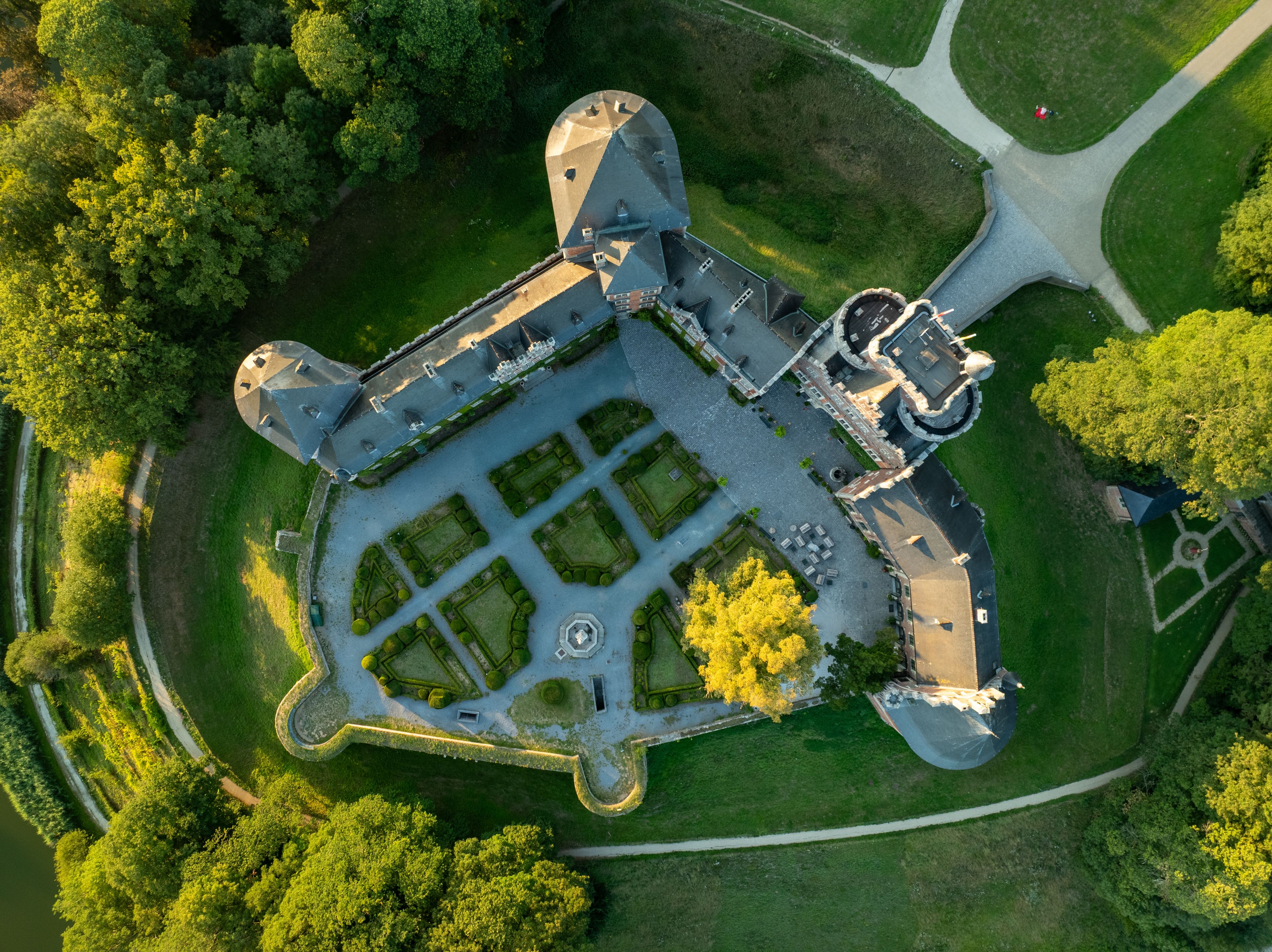 An aerial view of a historic building with a symmetrical layout, surrounded by a well-maintained garden and a moat.