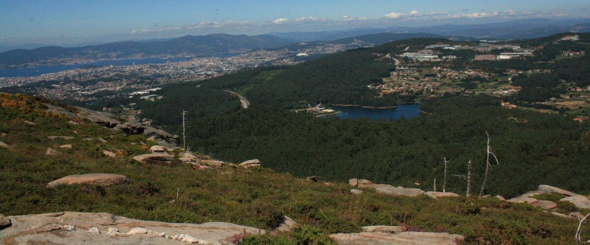 A mountainous landscape with a lake, forested areas, and distant cityscape.