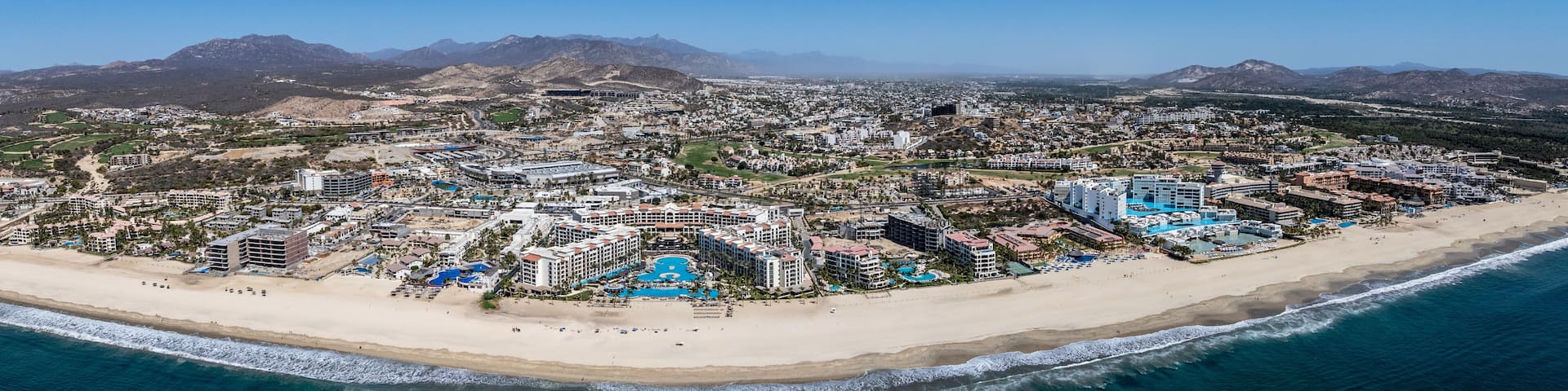 wide angle, panoramic aerial landscape view of Hotel Zone with white sand beach (Playa Hotelera) in San José del Cabo B.C.S., Mexico with many hotel close to beach and mountain landscape in background
