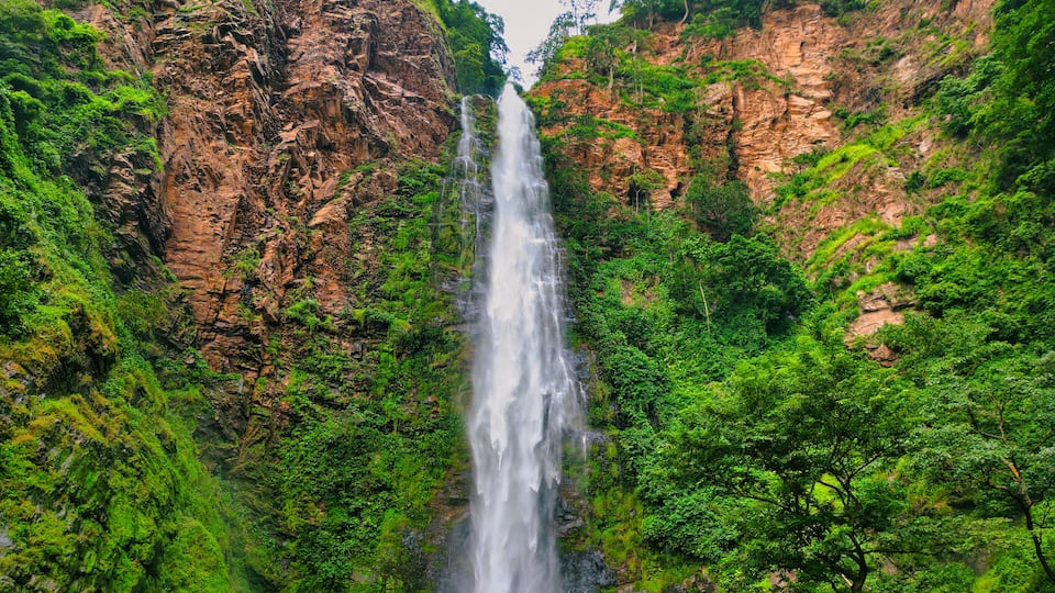 Aerial view of a powerful waterfall cascading down rugged cliffs, embraced by vibrant green vegetation, creating a breathtaking spectacle, Wli, Volta Region, Ghana.