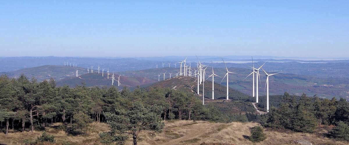A landscape with multiple wind turbines on a hill, surrounded by dense forests.
