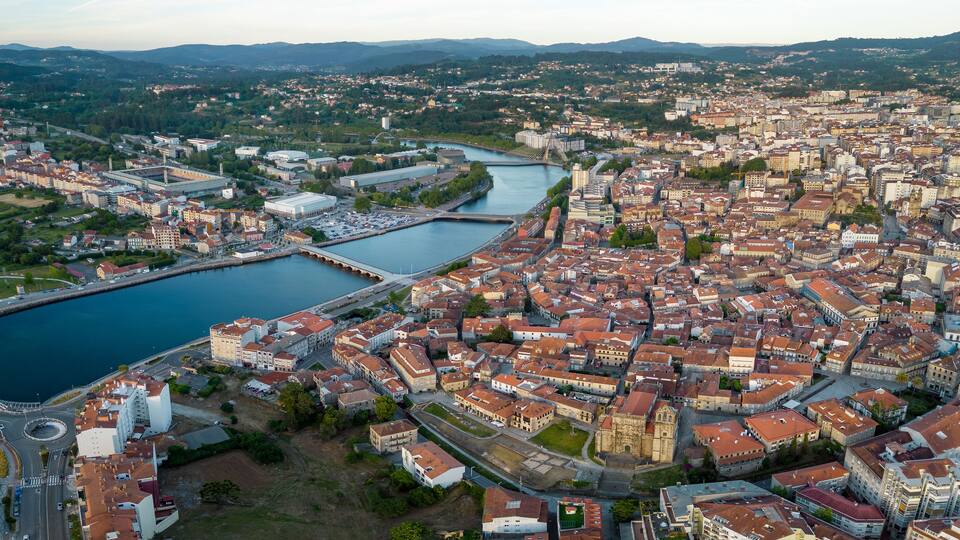 Vista aérea de una ciudad con río, puentes y montañas al fondo.