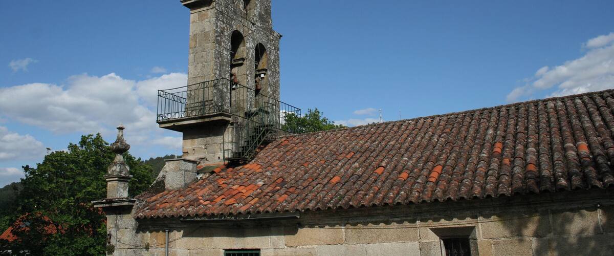 Uma torre de pedra histórica com telhado em telhas, cercada por árvores e céu claro.