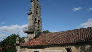 Una torre de piedra histórica con tejado de tejas, rodeada de árboles y un cielo despejado.