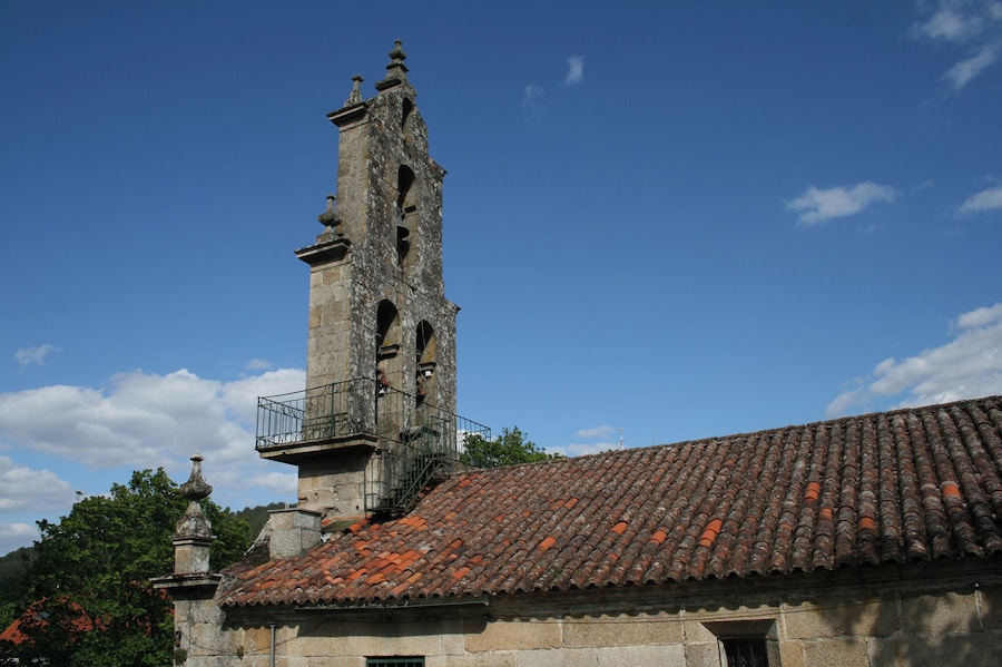 Una torre de piedra histórica con tejado de tejas, rodeada de árboles y un cielo despejado.