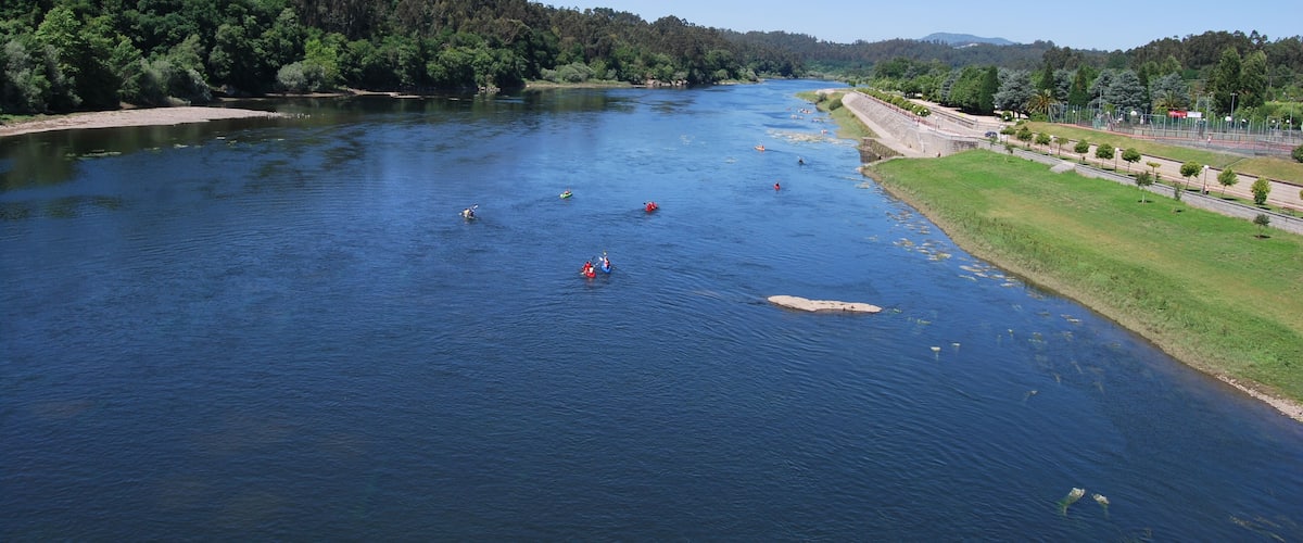 A river with kayaks, surrounded by dense forest and a paved path.