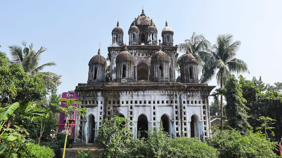 A historic temple with multiple domes and arches, surrounded by lush greenery and palm trees.