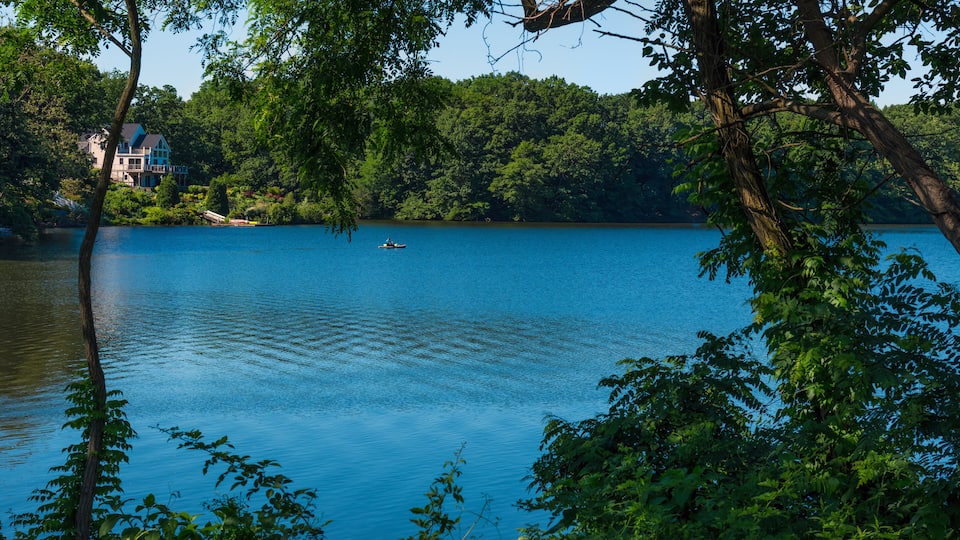 A calm lake surrounded by dense green forest and a large house on the shore.