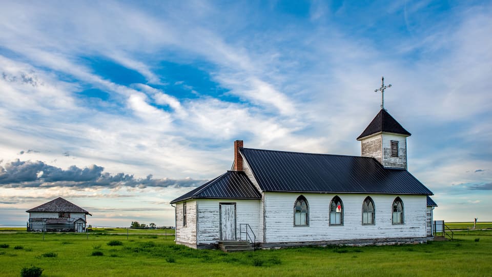 A white church with a steeple and a smaller building in a grassy field.