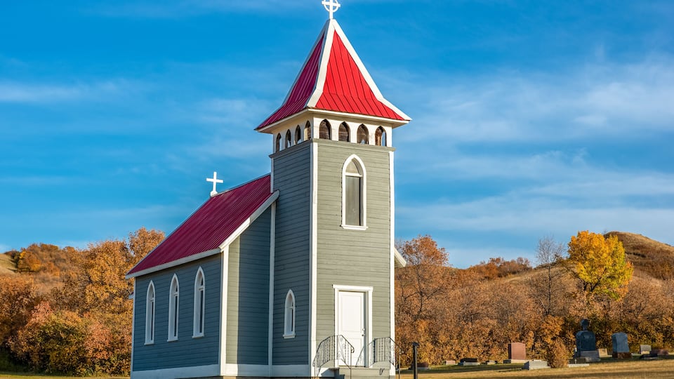 A church with a red roof and a white cross on top, surrounded by autumn trees.