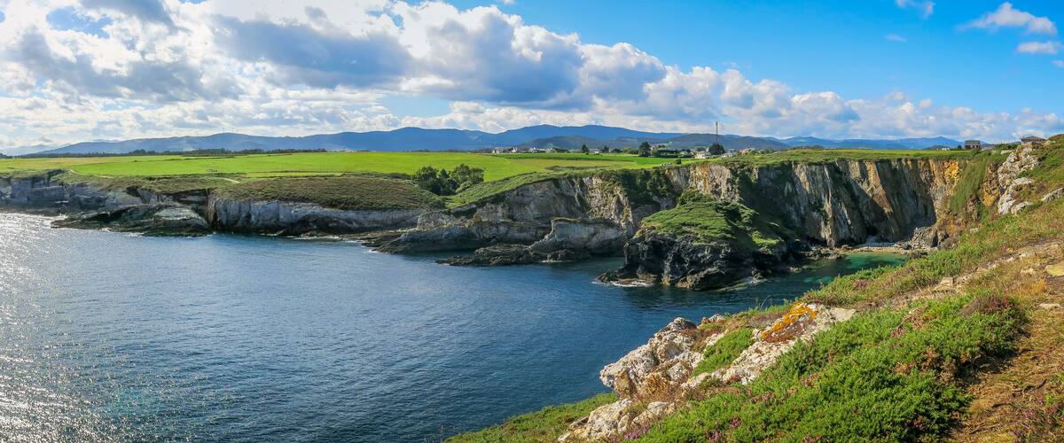 A coastal landscape with cliffs, a body of water, and distant mountains.