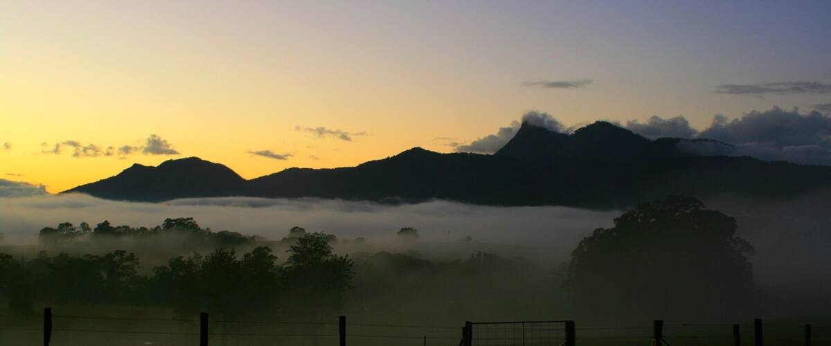 A sunrise over a mountainous landscape with a foggy valley and a fence in the foreground.