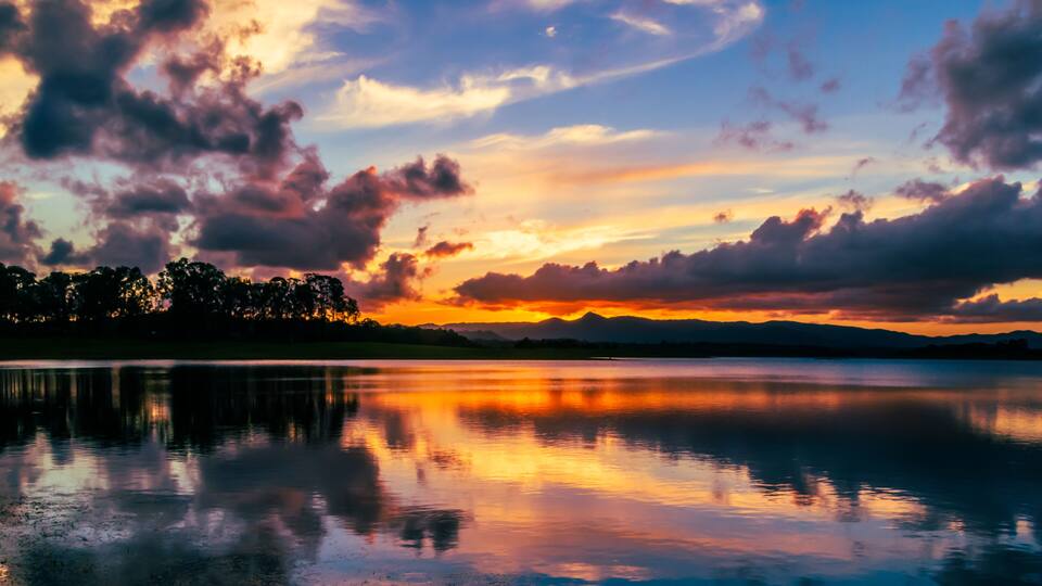 A sunset over a calm lake with mountains in the distance and a forested area along the water's edge.
