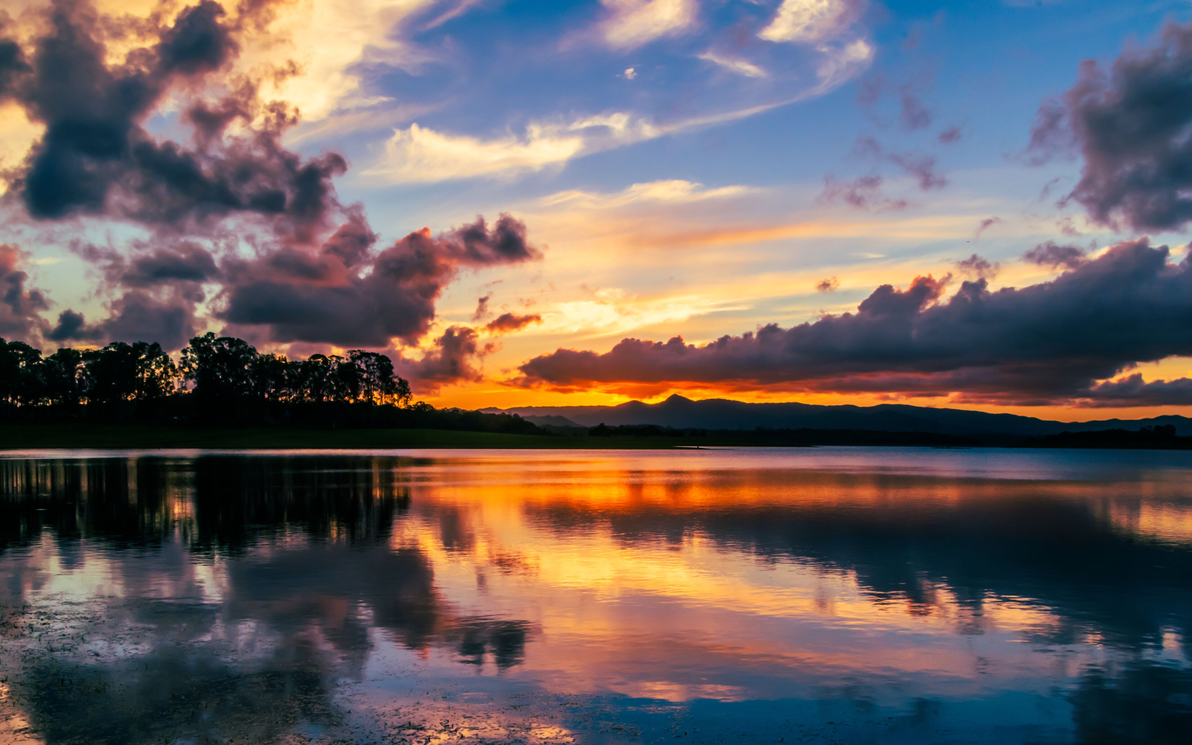 A sunset over a calm lake with mountains in the distance and a forested area along the water's edge.