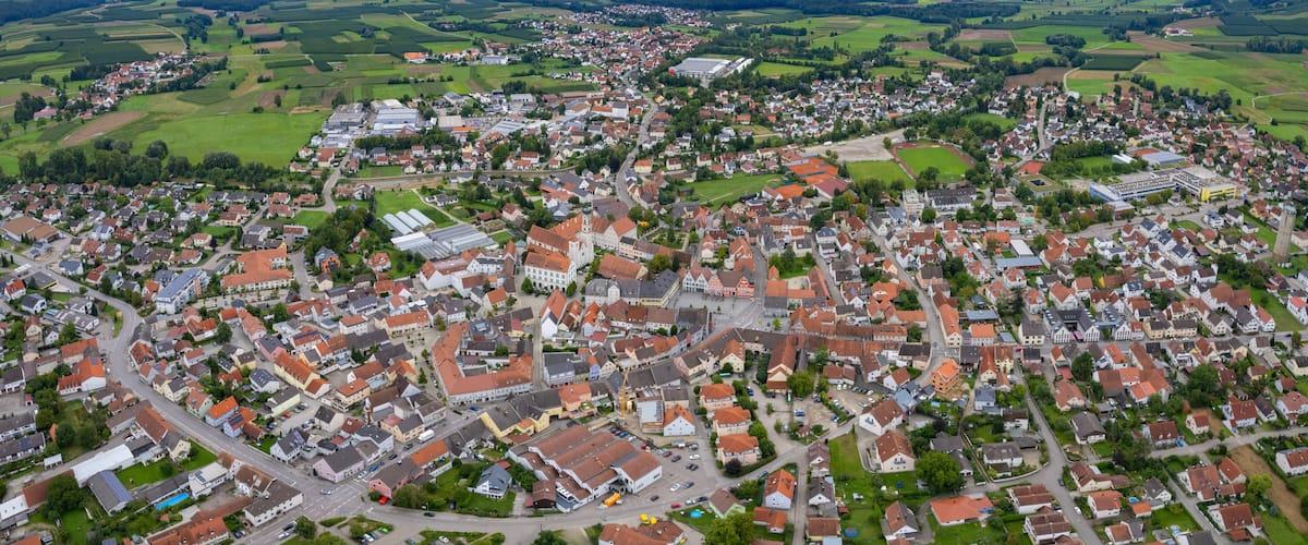 An aerial view of a town with a central square, surrounding houses, and green fields.