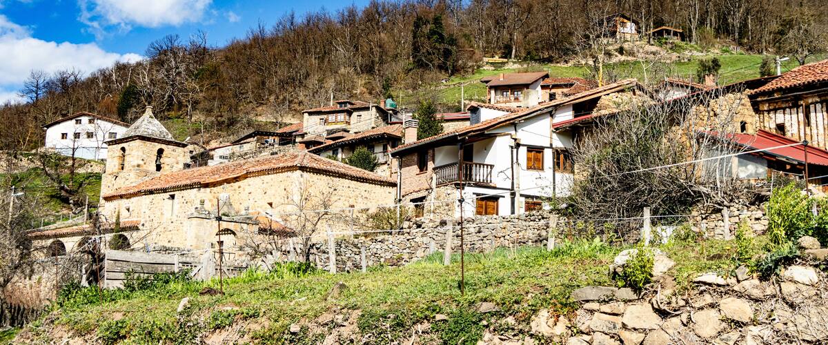 A hillside village with stone houses, a church, and a forested backdrop.