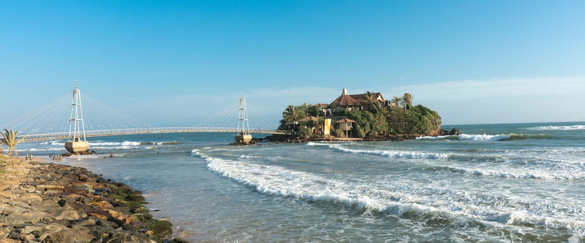 A coastal scene with a bridge, rocky shore, and a house on a small island.