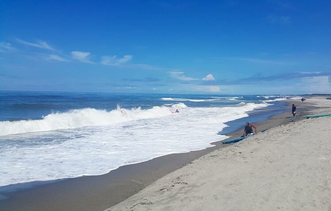 A beach with waves crashing onto the shore, a clear blue sky, and a few people on the sand.