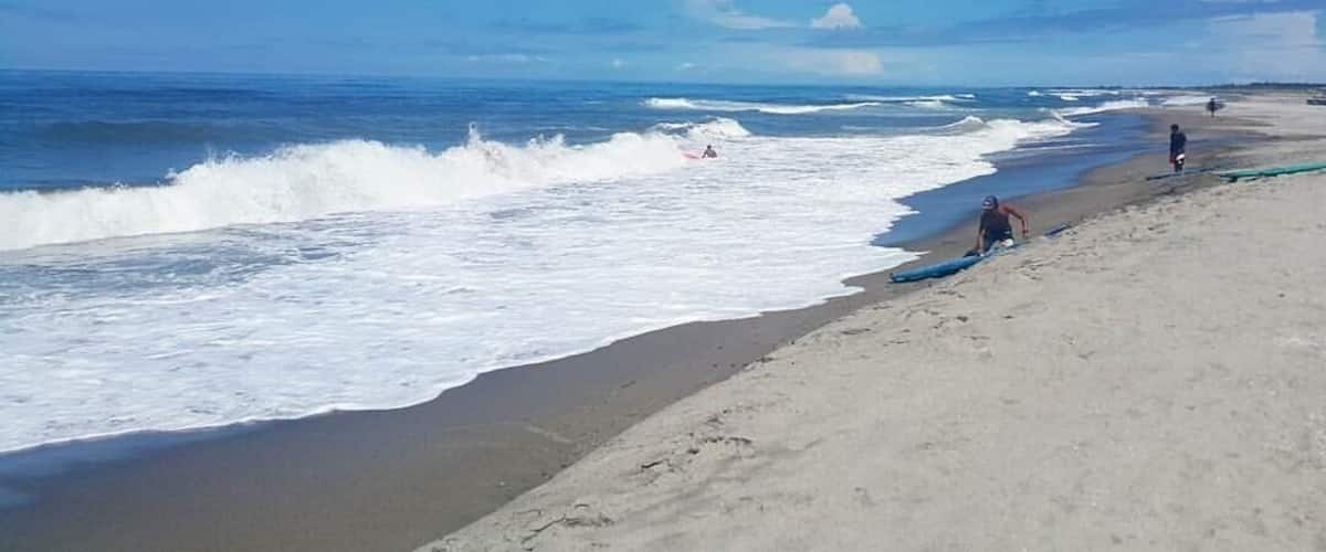 A beach with waves crashing onto the shore, a clear blue sky, and a few people on the sand.