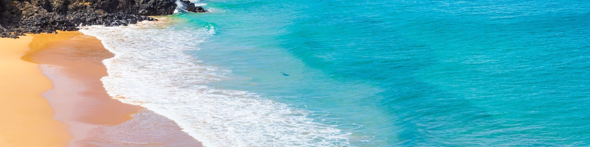 A beach with clear turquoise water, sandy shore, and rocky outcrops.