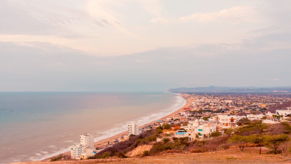 A coastal cityscape with a beach, buildings, and distant mountains.