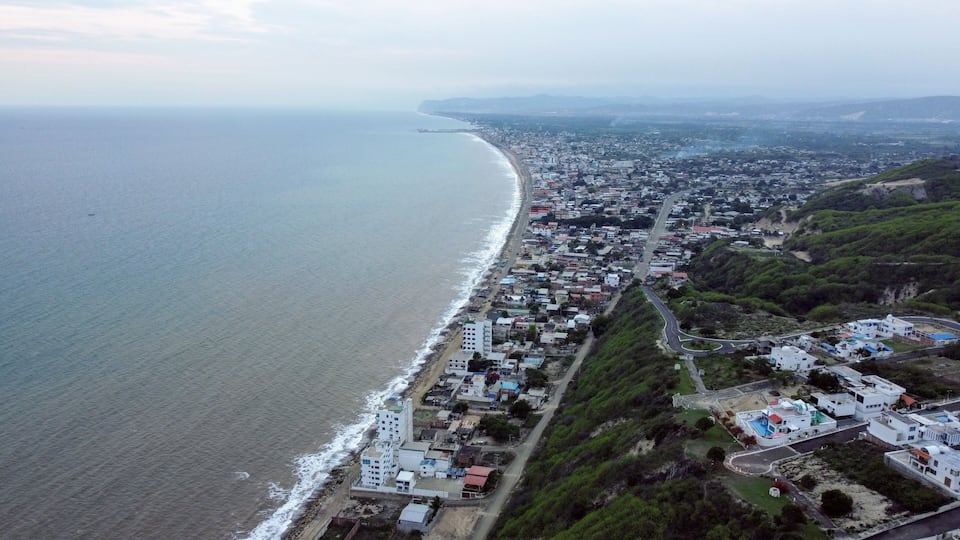 An aerial view of a coastal town with a long beach, dense housing, and a hilly landscape.