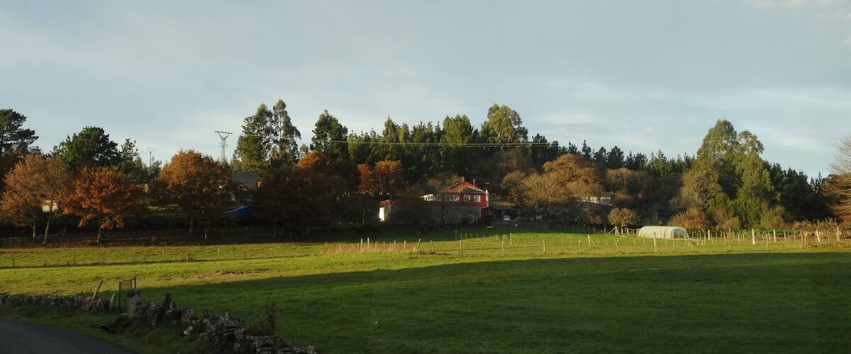 A rural landscape with a stone wall, a road, and a hill with trees and a house.
