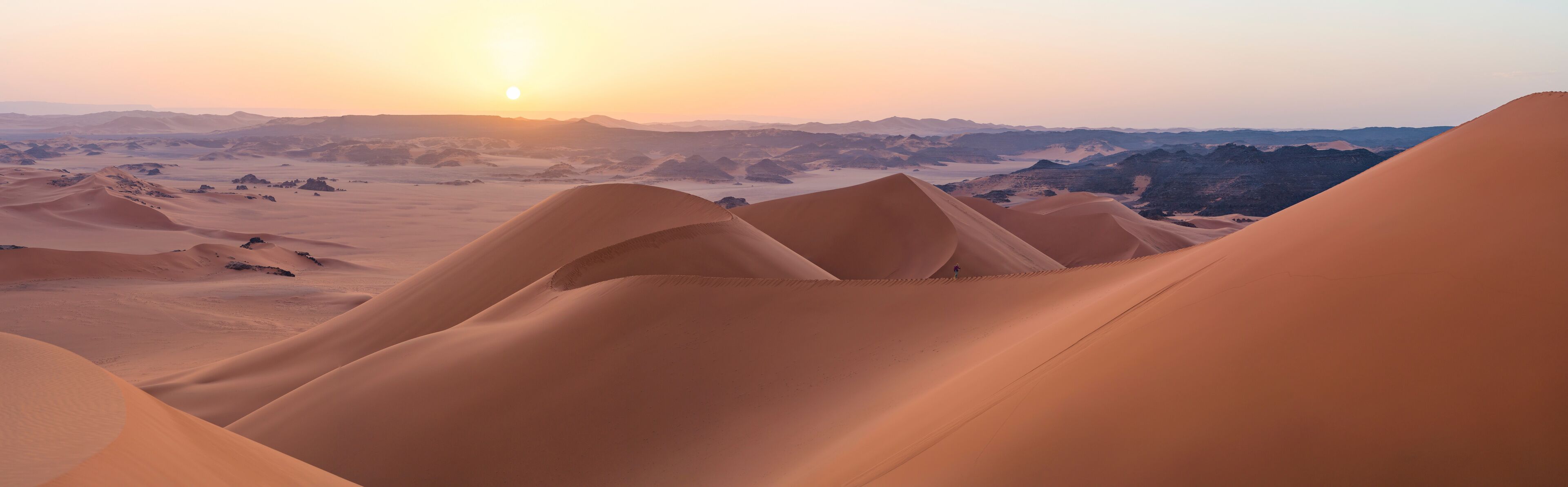 Sand dunes with a sunset in the background.