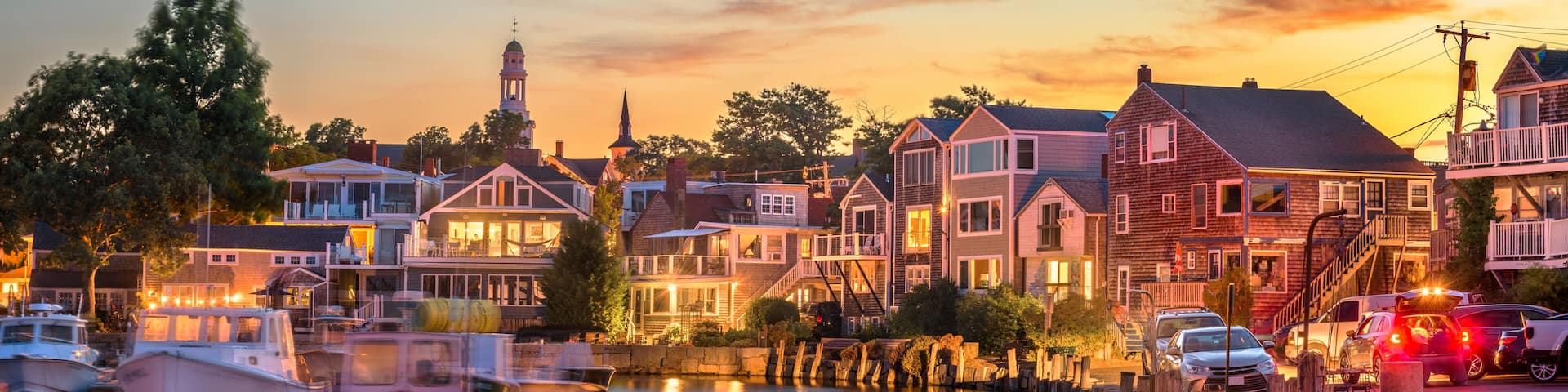 A harbor at dusk with boats, waterfront houses, and a church steeple.