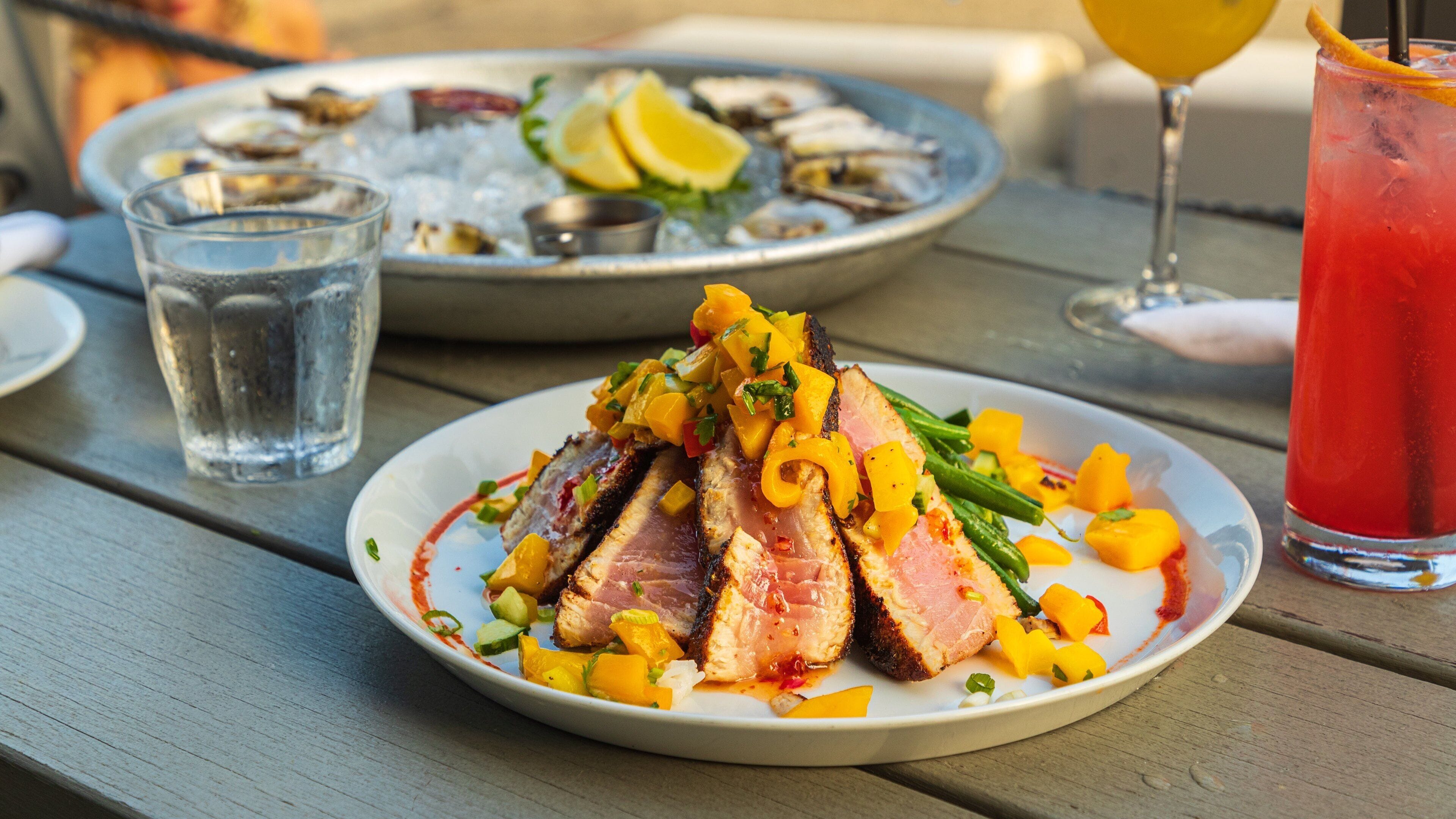 A plate of sliced meat with vegetables and a glass of red drink on a wooden table.