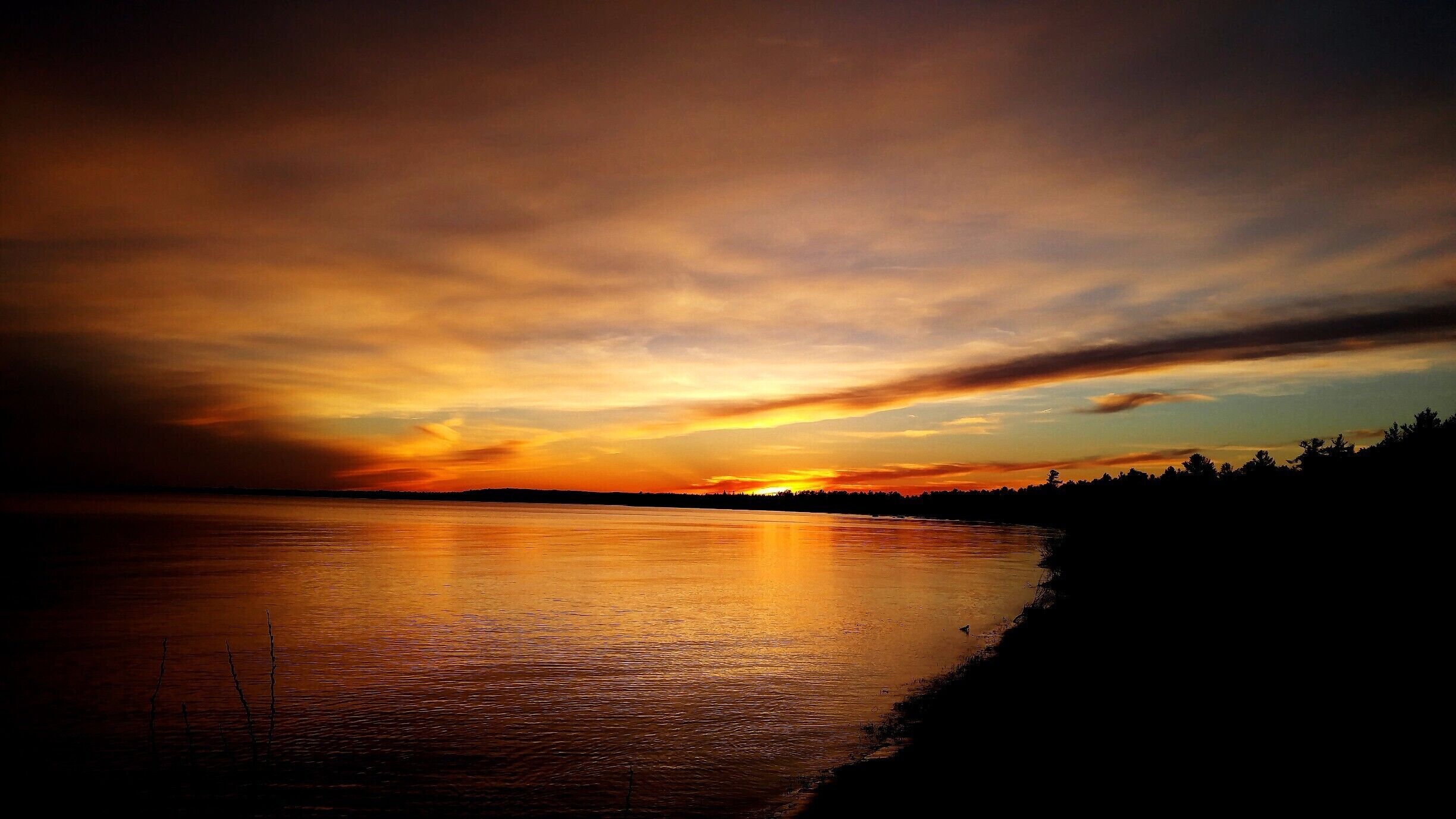A sunset over a calm lake with a silhouette of trees on the horizon.