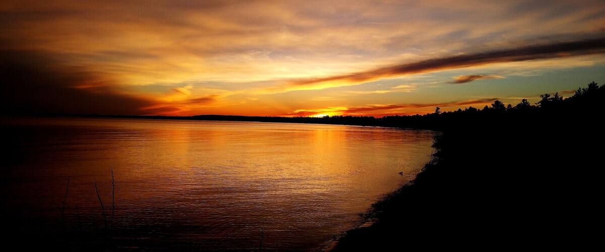 A sunset over a calm lake with a silhouette of trees on the horizon.