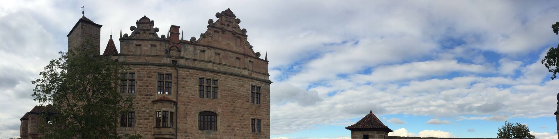 A historic stone castle with a round tower, surrounded by a stone wall and lush greenery.