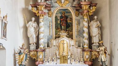 An ornate religious altar with statues, a central painting, and a white cloth-covered table.
