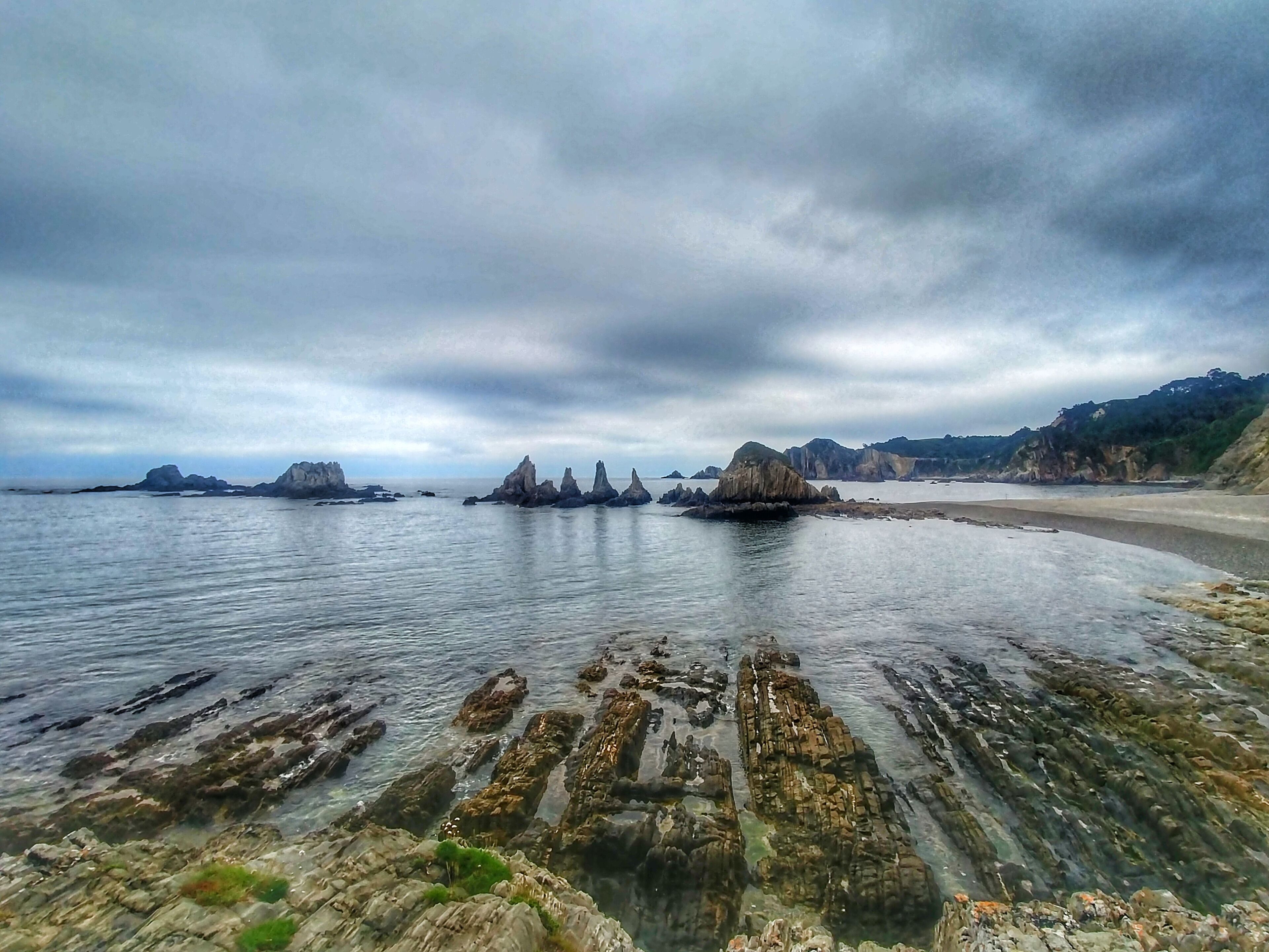 A coastal landscape with rocky formations and a sandy beach under a cloudy sky.