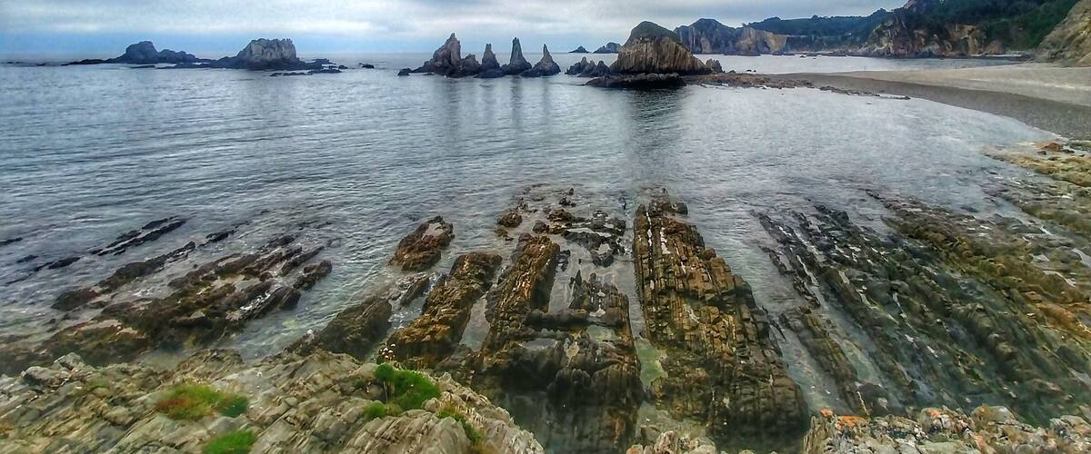 A coastal landscape with rocky formations and a sandy beach under a cloudy sky.