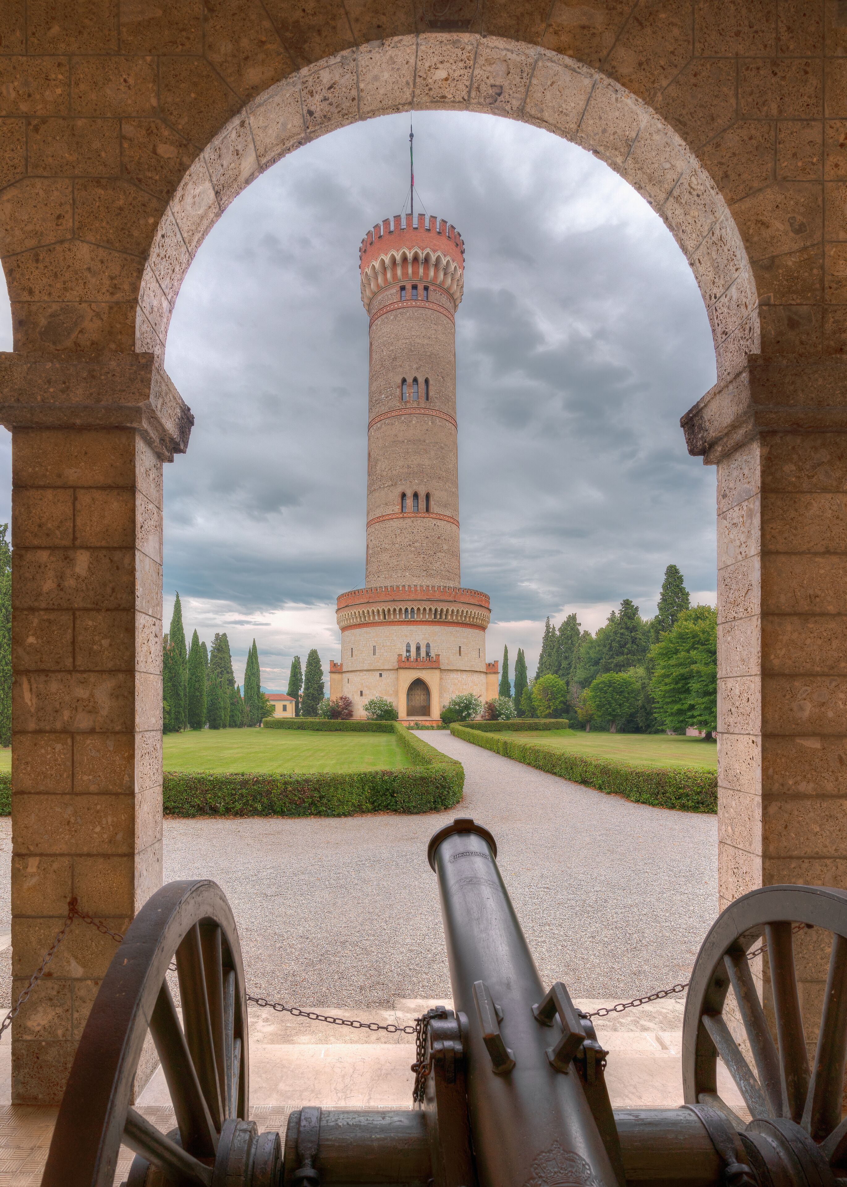 A historic tower with a crenellated top, viewed through an arched stone gateway.