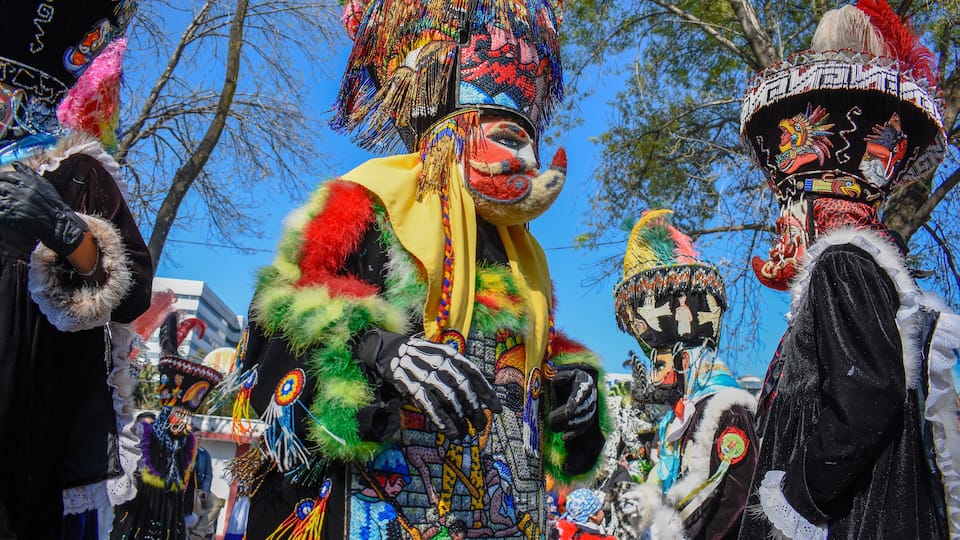 A person in a colorful, elaborate costume with a large, ornate headdress and a fur-trimmed outfit.