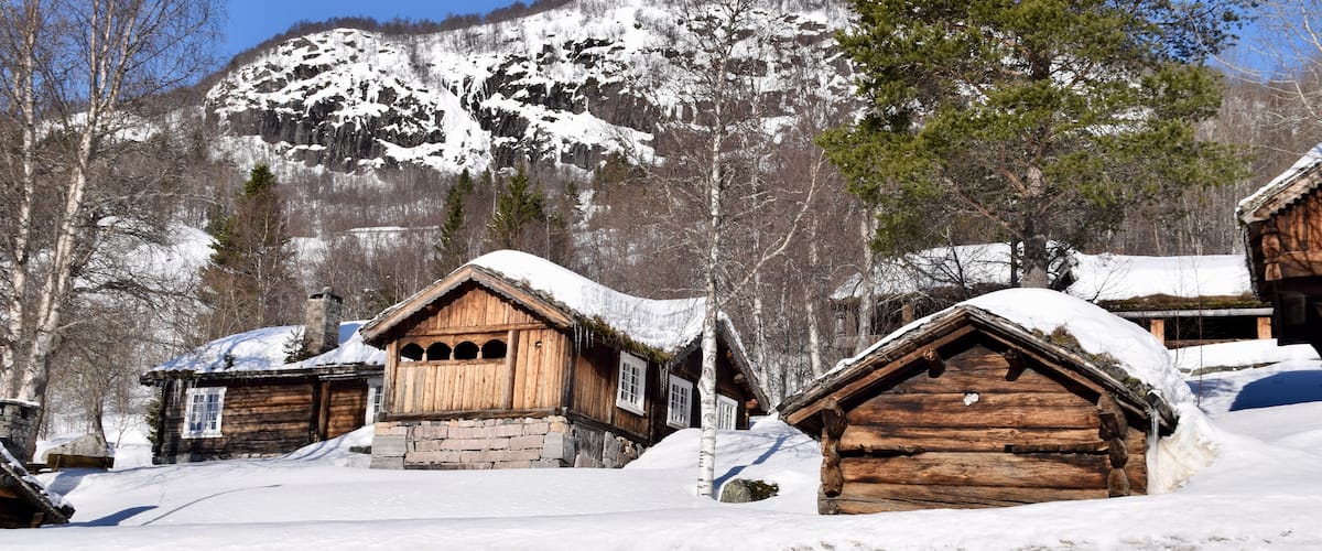 A snowy village with wooden houses and a mountain in the background.