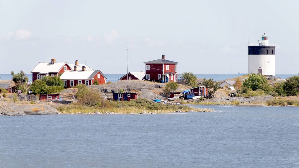 A coastal village with red houses, a lighthouse, and rocky terrain.