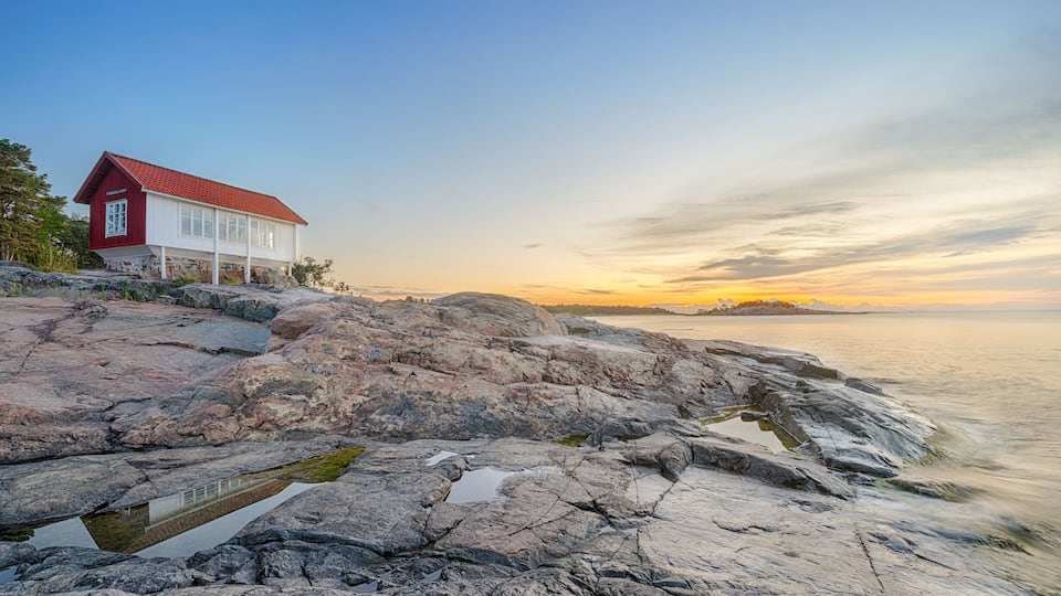 A red building on rocky terrain by the sea during sunset.