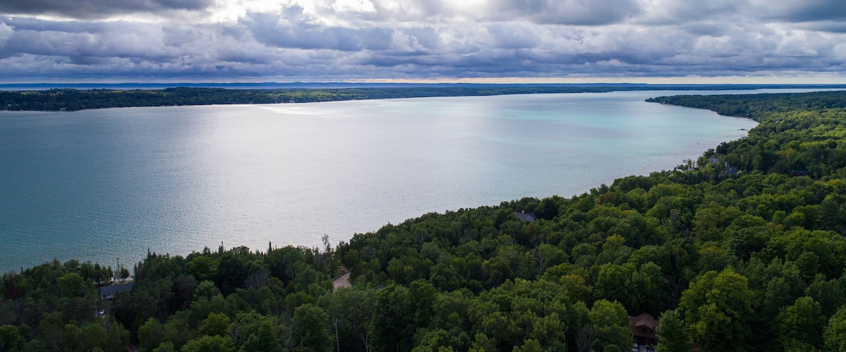 A large body of water surrounded by dense forest and a cloudy sky.