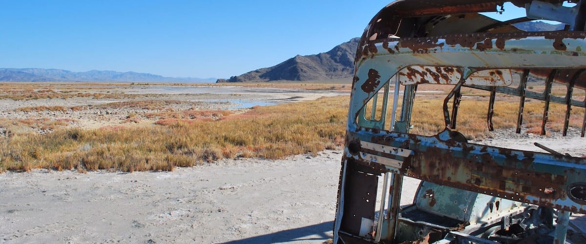 A rusted vehicle in a barren landscape with distant mountains.