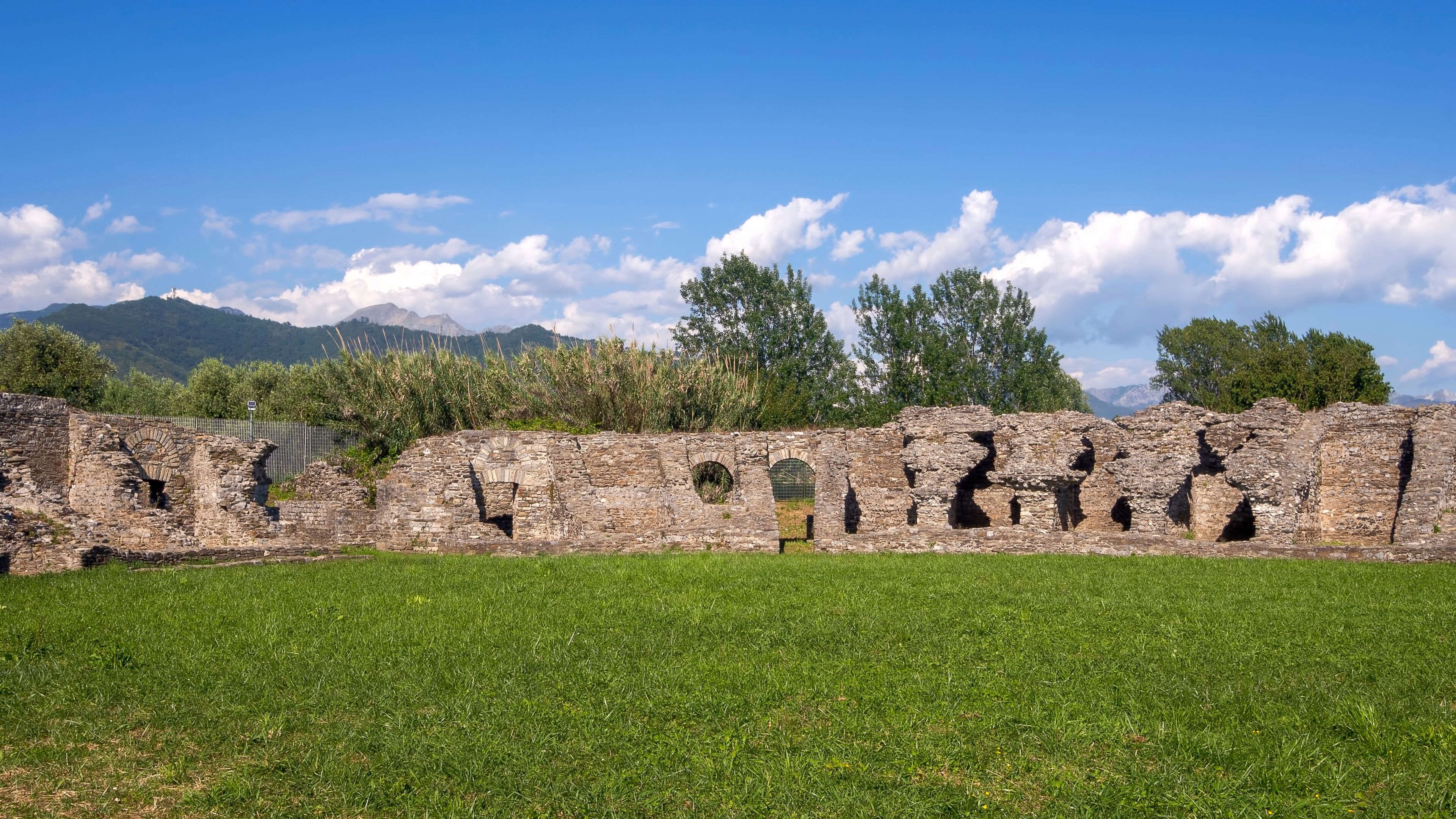 Ancient stone ruins with arched openings and a grassy field in the foreground.