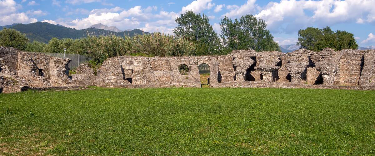 Ancient stone ruins with arched openings and a grassy field in the foreground.
